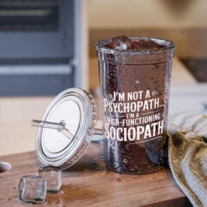 May include: A clear plastic tumbler with a silver lid and straw, filled with a dark liquid and ice cubes. The text on the tumbler reads: "I'M NOT A PSYCHOPATH... I'M A HIGH-FUNCTIONING SOCIOPATH."