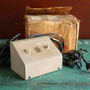 May include: A vintage gray metal foot pedal with two knobs and a cord. The pedal is labeled "Automatic Volume Control".