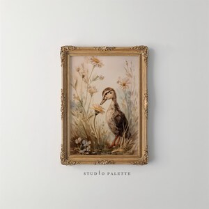 May include: A framed watercolor print of a duckling in a field of wildflowers. The duckling is brown and white with orange feet. The frame is gold with ornate detailing. The text "STUDIO PALETTE" is at the bottom.