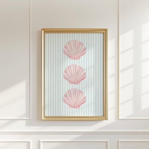 May include: A framed art print featuring three pink seashells arranged vertically on a light blue and white striped background. The seashells have detailed textures and are set against a watercolor-style backdrop. The frame is a thin, gold color.