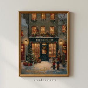 May include: A framed print of a cozy bookstore scene in winter. The shop, marked "THE BOOKSHOP," is adorned with Christmas decorations and warm interior lighting. Snow falls on the street, where two children stand with a bicycle, and a Christmas tree is on the left.