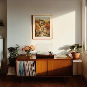 May include: A mid-century modern wooden record cabinet with a framed landscape print hanging above it. A turntable sits on top, next to a vase of roses and a potted plant. The cabinet doors are closed, and a collection of vinyl records is visible.