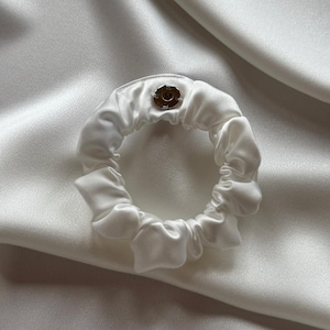 Könnte beinhalten: Ein weißer Satin-Haargummi mit einem kleinen silbernen Knopf.
