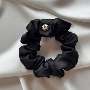 Könnte beinhalten: Schwarzes Satin-Haargummi mit einem silbernen Knopf.