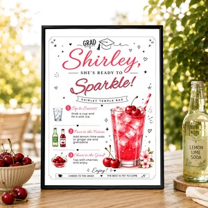 May include: A framed sign titled Grad Shirley, She's Ready to Sparkle! featuring a Shirley Temple bar recipe. The text includes instructions for a drink with lemon-lime soda, grenadine, and cherries, illustrated with a glass of red liquid.