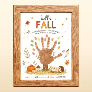 Può includere: Una cornice in legno contenente una stampa con il testo hello FALL, A little handprint, a little fall magic, and a whole lot of memories. Il centro presenta un'impronta di mano marrone a forma di albero, circondata da zucche, un fungo e un riccio.