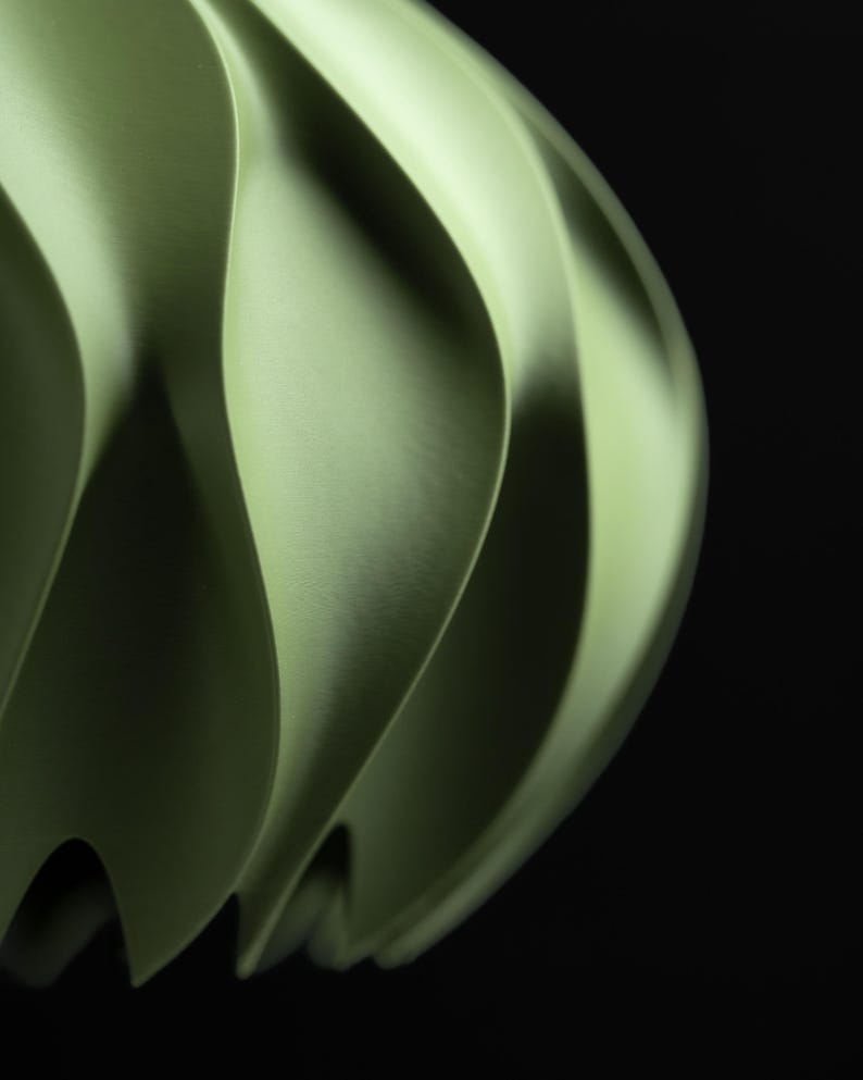 May include: A light green pendant light shade featuring a series of vertical, curved, and undulating fins that create a rhythmic, wave-like pattern. The structure has a smooth, matte finish and a rounded, bulbous form against a black background.
