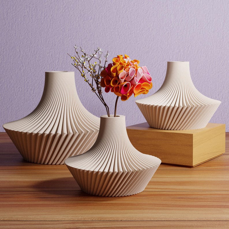 May include: Three cream-colored, geometrically designed vases with a ribbed texture. One vase holds a colorful flower arrangement with orange, pink, and white petals. The vases are arranged on a wooden surface with a light purple background.
