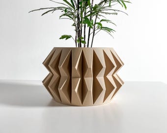 May include: A beige planter with a geometric, faceted exterior featuring repeating vertical diamond-shaped patterns. The pot has a wide, rounded base and a slightly narrower top opening, containing a green plant with thin, dark stems and leaves.