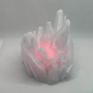 May include: A cluster of translucent white crystalline structures arranged in a jagged, pointed formation. The center of the cluster emits a bright, glowing red light that illuminates the inner facets of the white, semi-transparent material.