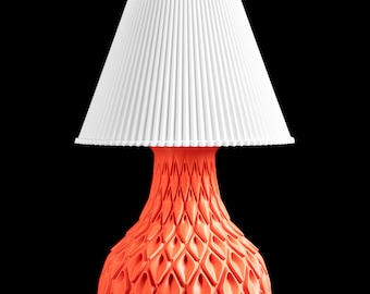 May include: A table lamp featuring a white, vertically pleated, conical lampshade atop a bright orange base with a complex, three-dimensional geometric pattern of repeating diamond-shaped indentations that create a textured, sculptural appearance.