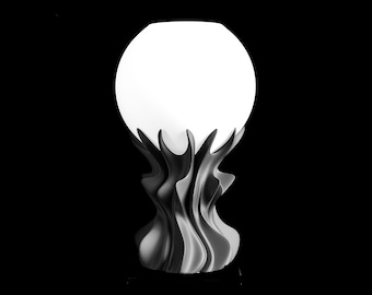 May include: A table lamp featuring a spherical white glass shade resting atop a dark gray, sculptural base with fluid, vertical, wave-like ridges that extend upward to cradle the bottom of the illuminated globe.
