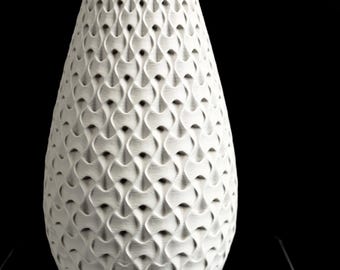 May include: A white vase with a repeating geometric pattern of interlocking, curved, and concave shapes across its entire exterior surface. The object has a tapered cylindrical form with a wide base and a slightly narrower top opening.