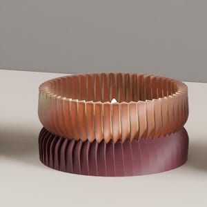 May include: A circular candle holder with a pleated, accordion-style exterior. The top section is a warm copper-orange color, while the bottom section is a deep, dark burgundy. A small, bright white candle flame is visible in the center.