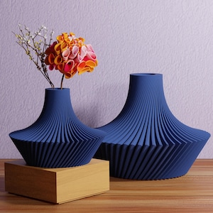 May include: Two navy blue decorative vases with a unique ribbed design. One vase holds a colorful flower arrangement with orange, pink, and yellow petals. The vases are on a wooden surface.