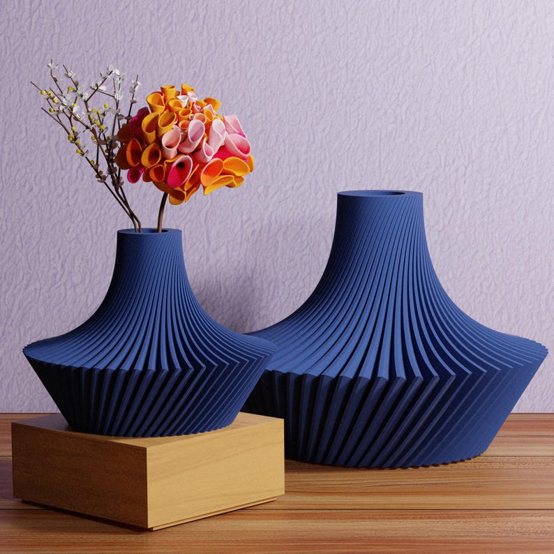 May include: Two navy blue decorative vases with a unique ribbed design. One vase holds a colorful flower arrangement with orange, pink, and yellow petals. The vases are on a wooden surface.