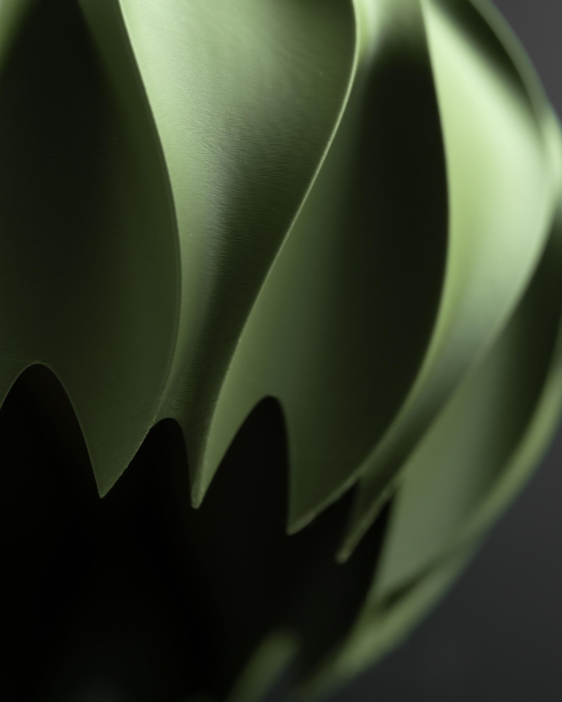 May include: A matte olive green object with a curved, spiraling, and layered structure. The surface features smooth, sweeping ridges that create deep shadows and sharp, pointed edges along the bottom, forming a complex, three-dimensional shape.
