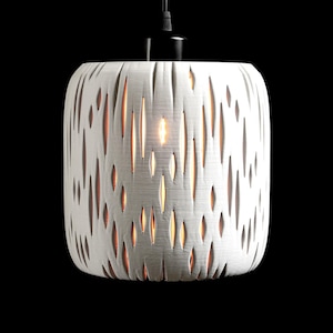 May include: A cylindrical pendant light fixture featuring a white exterior with vertical, elongated cutouts. The surface has a textured finish, and warm light glows from within the openings. It is suspended by a black cord and cap.