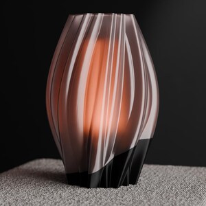 May include: A decorative vase with a unique, swirling design. The vase is a translucent, light brown color with vertical ridges. The base is black, and the interior glows with an orange light. The vase sits on a textured, gray surface.