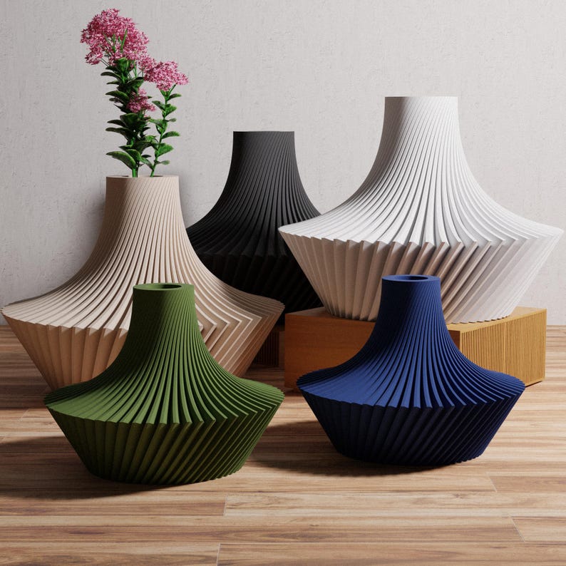 May include: A collection of modern, geometric vases in various colors, including beige, black, white, green, and blue. One vase holds pink flowers. The vases have a unique, ribbed design and are displayed on a wooden surface.