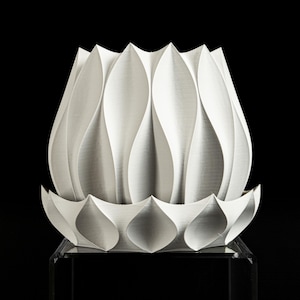 May include: A white, petal-shaped decorative object. The object has a layered design with a series of curved, pointed petals. The base of the object has a similar petal design. The object is displayed against a black background.