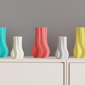 May include: A collection of five decorative vases in varying sizes and colors. The vases are teal, white, coral, gray, and yellow. Each vase has a unique, wavy design. They are displayed on a white surface against a gray background.
