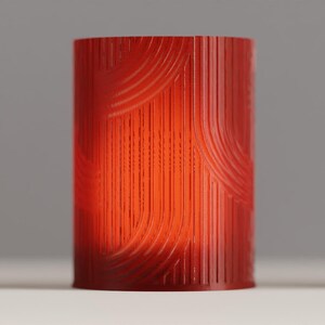 May include: A cylindrical red lamp shade featuring a textured surface with vertical and curved lines. The structure is translucent, allowing light to pass through the material, highlighting the intricate pattern of raised ridges across the exterior.