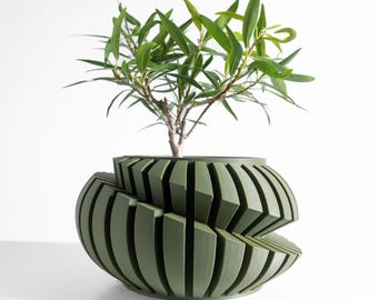 May include: A modern, olive green planter with a unique, geometric design. The planter is filled with a small tree with long, green leaves. The planter's design features vertical, angled slats that create a layered effect. The background is plain white.