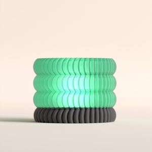 May include: A stack of three colorful hair ties. The bottom hair tie is dark gray, while the top two are a gradient of green. The hair ties have a ribbed texture and are stacked on top of each other.