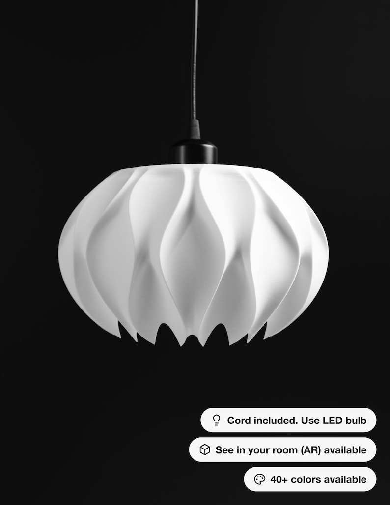 May include: A white pendant light fixture with a curved, petal-like structure suspended by a black cord. The fixture features a black top mount. Text on the image reads: Cord included. Use LED bulb, See in your room (AR) available, 40+ colors available.