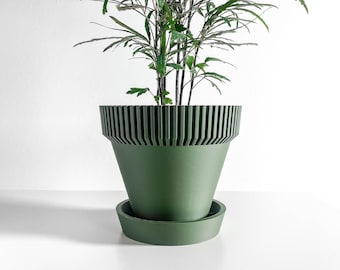 May include: A green plant pot with a matching saucer. The pot has a unique design with vertical lines around the top. The plant inside has green leaves and stems. The pot is sitting on a white surface.