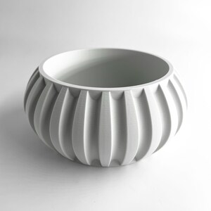 May include: A matte white bowl featuring a rounded, bulbous shape with prominent vertical fluted ridges extending from the base to the rim. The interior is smooth and hollow, while the exterior surface displays a consistent ribbed texture.