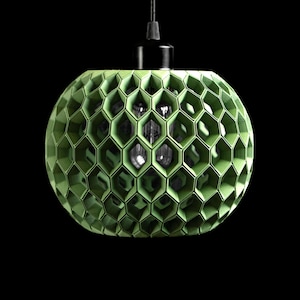 May include: A green, spherical pendant light with a honeycomb design. The light fixture is suspended from a black cord and has a black fixture at the top. The geometric pattern creates a unique, modern aesthetic. The background is black.