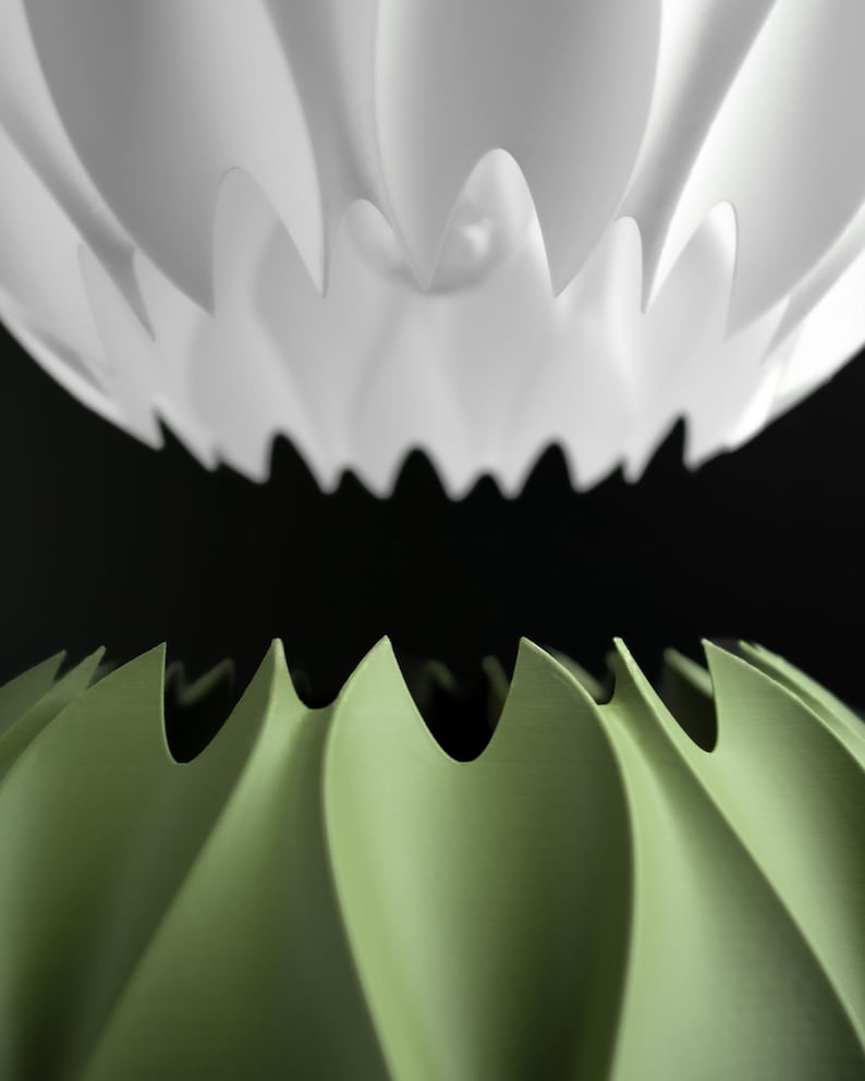 May include: A white and a light green pendant lamp shade, each featuring a series of deep, vertical, pointed pleats that create a sharp, serrated edge. The two shades are positioned vertically, one above the other, against a black background.
