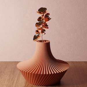 May include: A matte terracotta-colored vase with a wide, ribbed, spiraling base and a narrow neck. A metallic, reflective copper-toned branch with multiple small, rounded, petal-like shapes extends upward from the center of the vase opening.