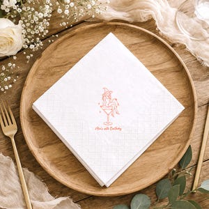 May include: A square white paper napkin featuring a copper-colored line art illustration of a witch sitting in a martini glass. Below the illustration, the text reads Mia's 30th Birthday in a matching copper-colored script font.