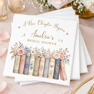 May include: A stack of white paper napkins featuring a gold printed design with the text A New Chapter Begins Amelia's BRIDAL SHOWER. The illustration shows a row of colorful vintage books topped with a variety of pastel floral arrangements.