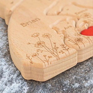 Puede incluir: Una tabla de cortar de madera en forma de coraz&oacute;n con los nombres "Brian" y "Ava" grabados. Delicados dise&ntilde;os florales est&aacute;n grabados en los bordes. Se ve un peque&ntilde;o coraz&oacute;n rojo. La tabla es de madera clara.