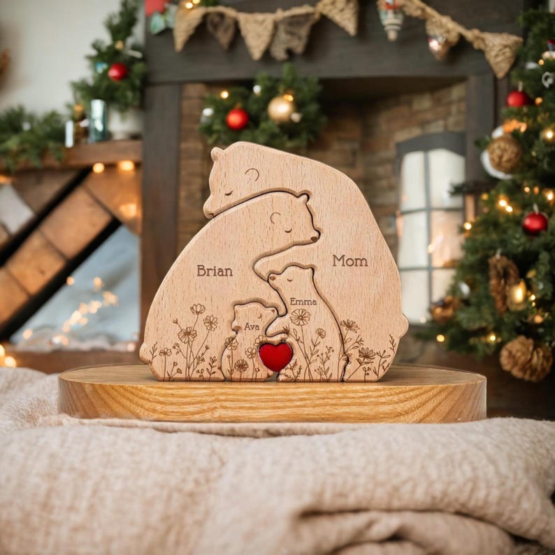 Puede incluir: Rompecabezas de madera de una familia de osos con los nombres "Brian", "Mom", "Emma" y "Ava" grabados. El rompecabezas presenta un coraz&oacute;n rojo y detalles florales. Los osos est&aacute;n apilados, simbolizando la familia. El rompecabezas se muestra sobre un soporte de madera.
