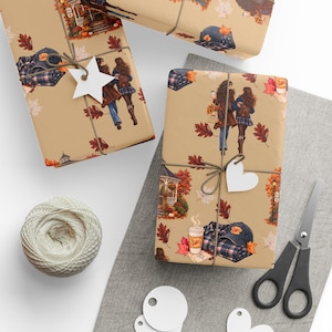 May include: Wrapping paper featuring a repeating autumn pattern on a tan background. The design includes illustrations of two people walking, a gazebo, a coffee cup labeled Luke's, a plaid shirt, and a baseball cap with the text Luke's, all surrounded by fall leaves.