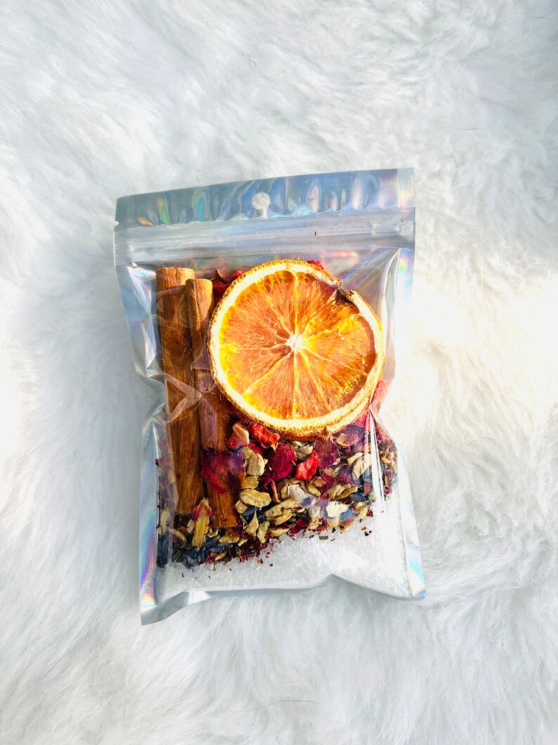 May include: A clear plastic bag filled with a mix of dried orange slices, cinnamon sticks, and other spices. The bag is sealed and ready to be used for making a festive drink.