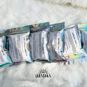May include: Five iridescent holographic pouches with text that reads "Abundance Simmer Pot", "Blessing Simmer Pot", "Protection Simmer Pot", "Apple Cinnamon Simmer Pot", and "Chai Vanilla Simmer Pot".