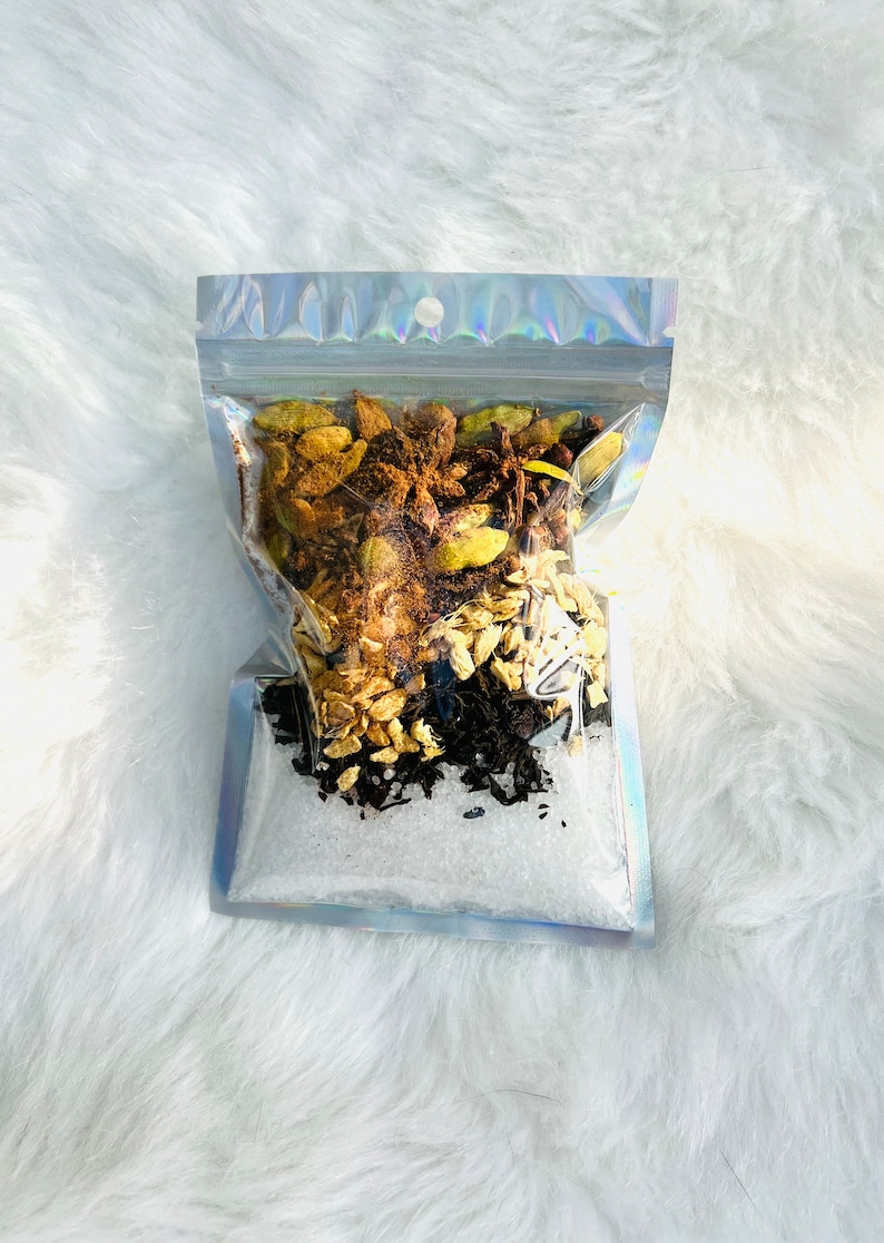 May include: A clear plastic bag filled with a blend of spices, including cardamom pods, star anise, ginger, and black tea. The spices are arranged in layers, with the cardamom pods at the top and the black tea at the bottom.