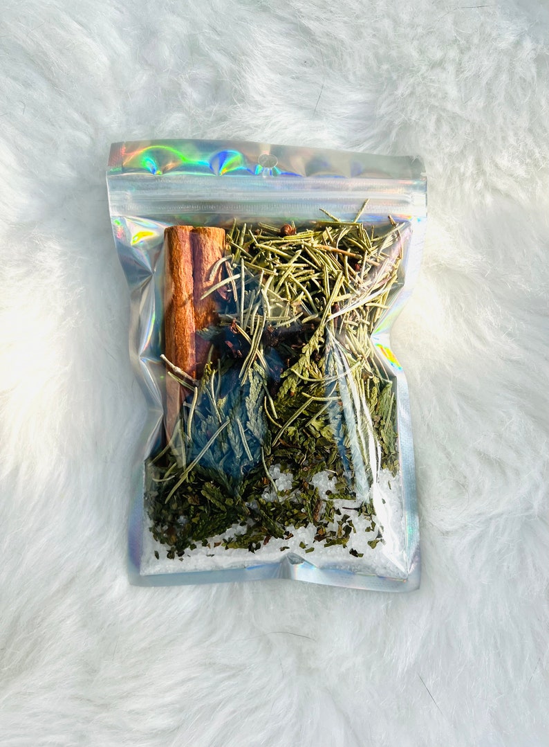 May include: A clear plastic bag filled with a blend of dried herbs and spices, including cinnamon sticks, green leaves, and white salt crystals.