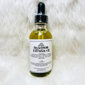 Può includere: Una bottiglia di vetro trasparente con un contagocce nero riempita con un liquido giallo. L'etichetta recita "PERSEPHONE DIFFUSER OIL" ed elenca gli ingredienti e il sito web del negozio Celstars. La bottiglia contiene 59 ml di olio.