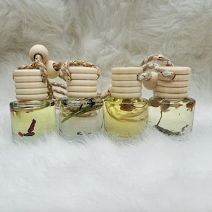 May include: Four small glass bottles with wooden tops and string hangers. The bottles are filled with a clear liquid and contain dried flowers and herbs.