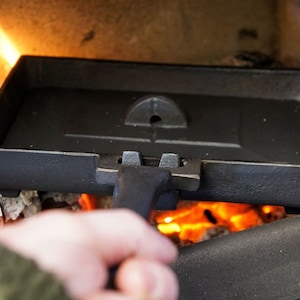 May include: A black cast iron pan with a handle, being held over a fire. The pan has a small hole in the centre.