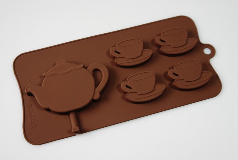 May include: Brown silicone mold for making chocolate teacups and a teapot. The mold has four teacup and saucer molds and one teapot mold.
