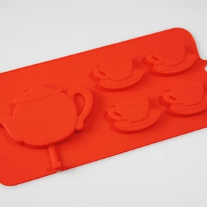 May include: Red silicone mold for making chocolate or candy in the shape of a teapot and four teacups.