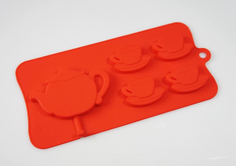 May include: Red silicone mold for making chocolate or candy in the shape of a teapot and four teacups.